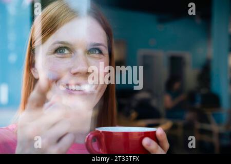 Donna sorridente che tiene una tazza di caffè al bar Foto Stock