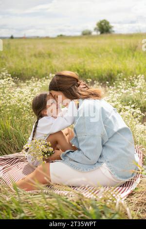 Figlia sorridente che abbraccia la madre seduta al campo Foto Stock
