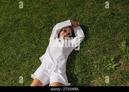 Ragazza sorridente che indossa occhiali da sole sdraiata sull'erba Foto Stock