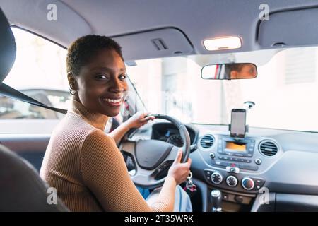 Giovane donna sorridente che tiene il volante in auto Foto Stock