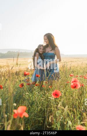 Madre e figlia si abbracciano a vicenda in campo di papavero Foto Stock