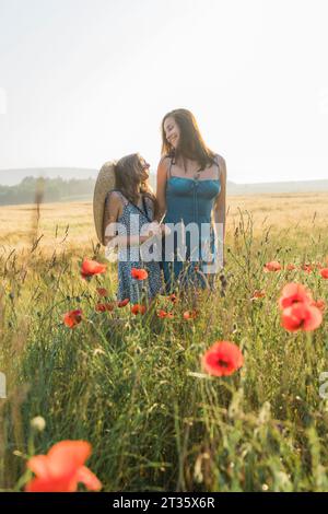Madre e figlia sorridenti che trascorrono il tempo libero in un campo di papavero Foto Stock