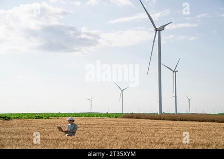 Agricoltore che lavora su un computer portatile in un campo di grano nelle giornate di sole Foto Stock