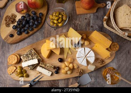Formaggi assortiti su una tavola di legno, in stile rustico. Diversi formaggi a fette con pere, pesche, uva, olive, miele, pane, cracker e noci. Selez Foto Stock