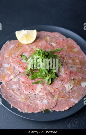 Carpaccio di manzo marmorizzato con rucola, parmigiano, olio d'oliva e limone. Un tradizionale antipasto classico a base di carne cruda tagliata a fette sottili. Primo piano, Foto Stock