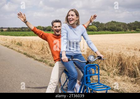 Uomo felice che si diverte con una donna che va in bicicletta vicino al campo Foto Stock