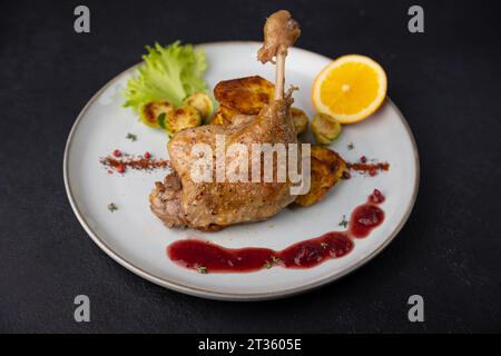 Confit di coscia d'anatra con germogli di Bruxelles, patate al forno, timo, arancia e salsa di mirtilli. Cucina francese tradizionale. Messa a fuoco selettiva, primo piano, bla Foto Stock