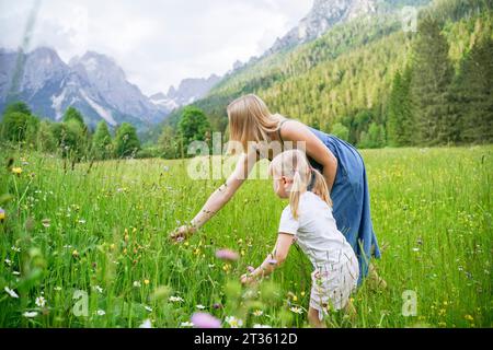 Donna che raccoglie fiori con figlia in piedi tra le piante Foto Stock