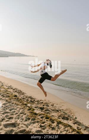 Donna che salta davanti al mare in spiaggia Foto Stock