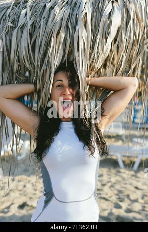 Donna allegra in spiaggia sotto l'ombrellone di paglia Foto Stock