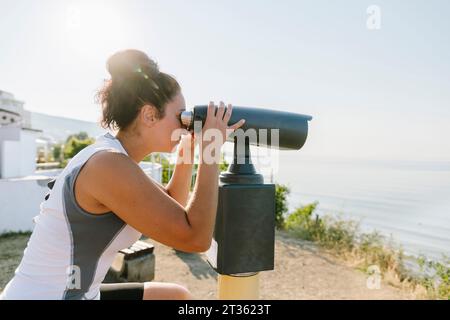 Donna che guarda attraverso un binocolo stazionario nelle giornate di sole Foto Stock