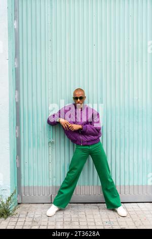 Persona non binaria che indossa occhiali da sole davanti alla porta blu Foto Stock