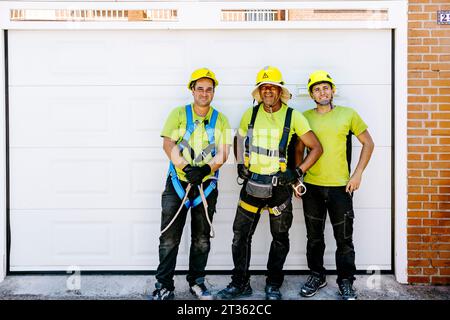 Tecnici soddisfatti che indossano cappelli resistenti davanti alla porta del garage Foto Stock