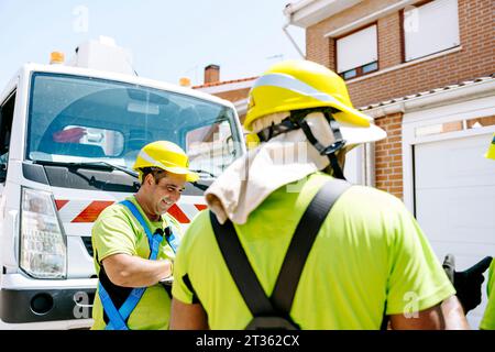 Tecnici soddisfatti che indossano cappelli resistenti davanti al veicolo Foto Stock