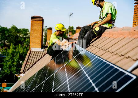 Ingegnere seduto sul tetto con un collega che installa un pannello solare Foto Stock