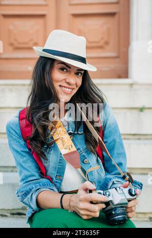 Donna felice che indossa un cappello seduto con la macchina fotografica Foto Stock