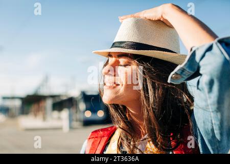 Giovane donna sorridente che indossa un cappello con gli occhi chiusi nelle giornate di sole Foto Stock