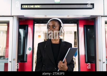 Donna premurosa che indossa cuffie e si trova in piedi con un computer portatile davanti alla metro Foto Stock