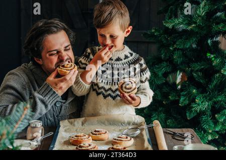 Padre e figlio mangiano panini alla cannella a tavola Foto Stock