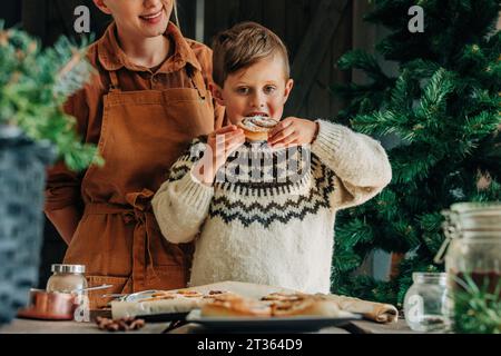 Figlio che mangia panino alla cannella a tavola Foto Stock