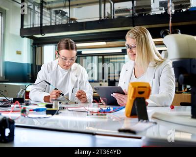 Scienziato sorridente che misura la scheda stampata con un collega utilizzando un tablet PC Foto Stock