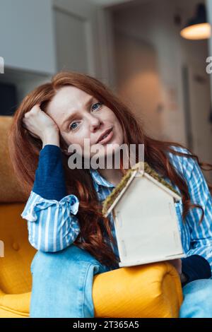 Donna rossa seduta con casa modello a casa Foto Stock