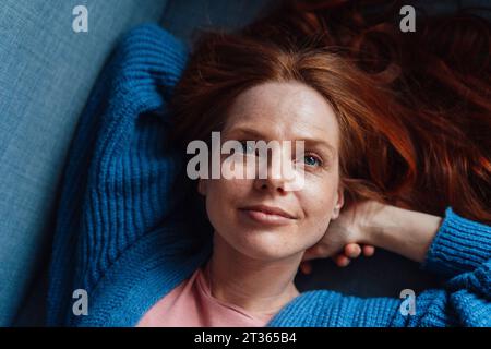 Donna sorridente a testa rossa che si rilassa sul divano Foto Stock