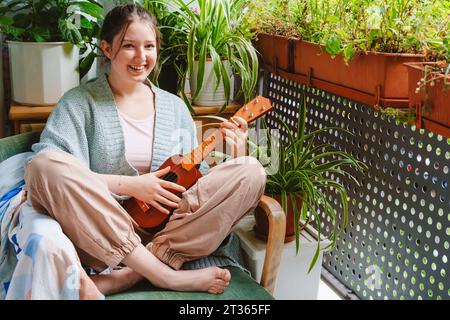 Bella ragazza adolescente con ukulele seduto sulla sedia sul balcone Foto Stock