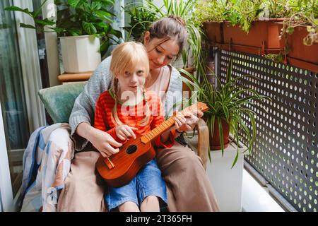 Ragazza adolescente che insegna alla sorella a giocare a ukulele sul balcone Foto Stock