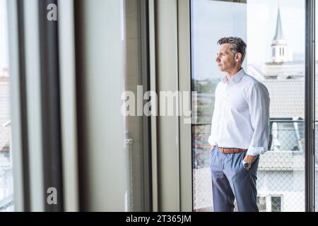 Un uomo d'affari maturo e premuroso in piedi accanto alla finestra in ufficio Foto Stock