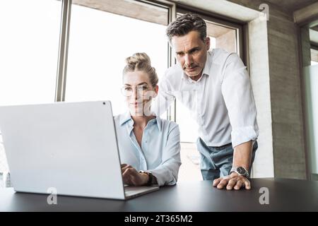 Uomo d'affari maturo con donna d'affari che usa un computer portatile alla scrivania Foto Stock