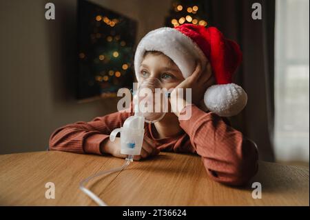 Ragazzo contemplativo che usa inalatore seduto al tavolo Foto Stock