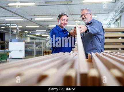 Falegname sorridente che tiene una tavola di legno con il tirocinante in fabbrica Foto Stock