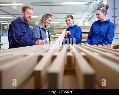 Tirocinante sorridente che tiene una tavola di legno in fabbrica Foto Stock