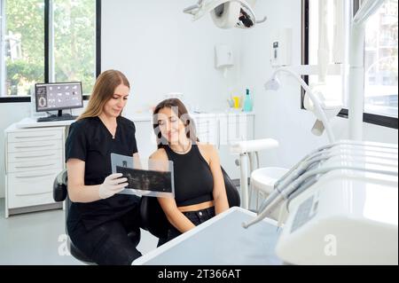 Giovane dentista che mostra raggi X al paziente nella sala esame Foto Stock