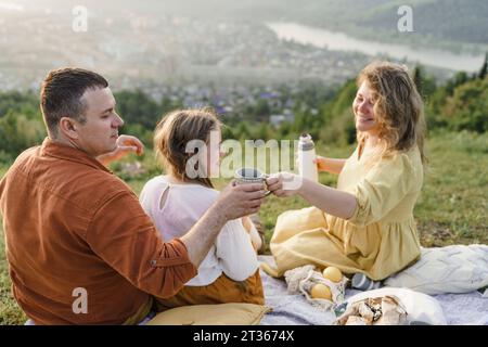 Donna felice che serve tè all'uomo seduto con una figlia Foto Stock