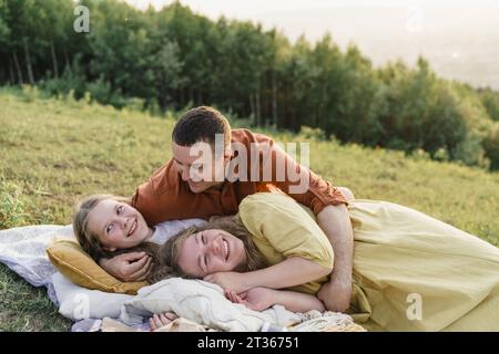 Famiglia sorridente che si diverte a sdraiarsi su una coperta nel prato Foto Stock