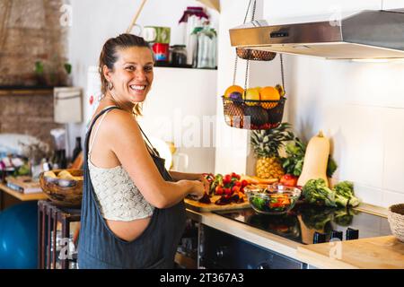 Donna incinta sorridente che prepara l'insalata in cucina a casa Foto Stock