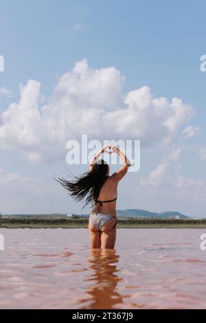 Donna spensierata che mostra segni cardiaci e si trova nel lago sotto il cielo Foto Stock