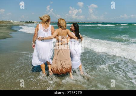 Amici con le braccia che camminano insieme sulla spiaggia Foto Stock