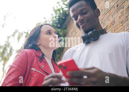 Donna sorridente con un uomo che usa il telefono cellulare Foto Stock
