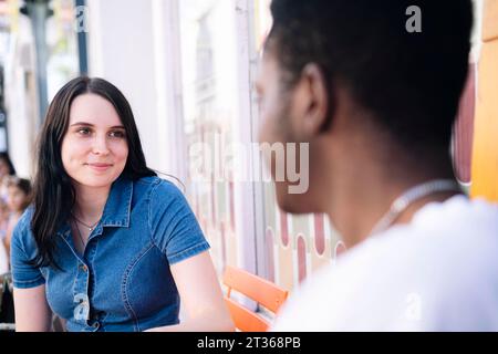 Giovane donna sorridente seduta con un uomo nel caffè sul marciapiede Foto Stock