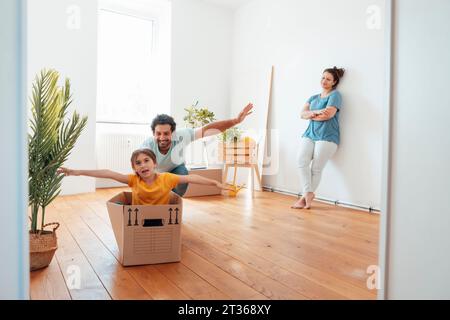 Buon padre che gioca con la figlia seduta in una scatola di cartone sul pavimento a casa Foto Stock