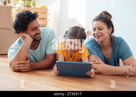 Donna felice e uomo con figlia che usa un tablet PC sul pavimento Foto Stock