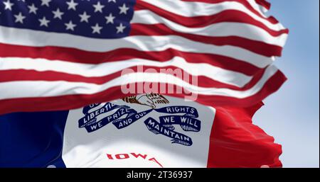Primo piano della bandiera dello stato dell'Iowa che sventola al vento con la bandiera nazionale americana in una giornata limpida. rendering dell'illustrazione 3d. Tessuto ondulato. Messa a fuoco selettiva Foto Stock