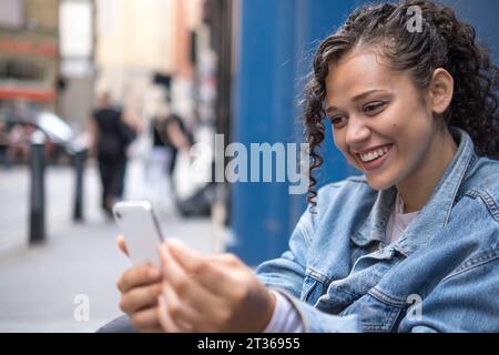 Giovane donna felice che usa lo smartphone sul sentiero Foto Stock