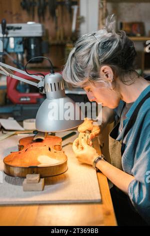 Liutaio che lavora su una parte del violino a ponte alla scrivania in officina Foto Stock