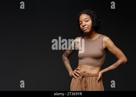 Donna sorridente con tatuaggio e cicatrici di acne in piedi su sfondo nero Foto Stock