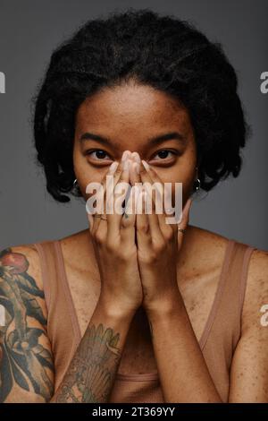 Giovane donna che copre il viso con le mani su sfondo grigio Foto Stock