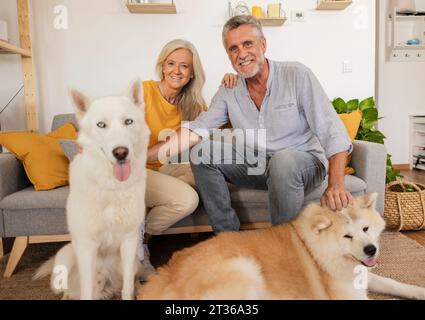 Felice coppia seduta sul divano con i cani a casa Foto Stock